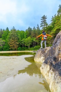 Female hiker standing on rock with open arms, enjoying the serene view of the inlet and lush forest