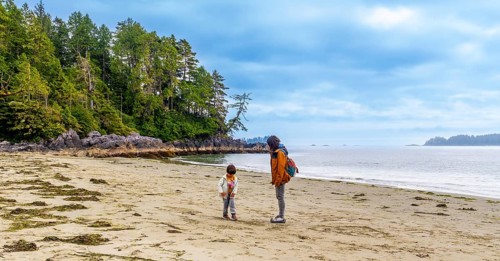 Tourists enjoying a leisurely walk along mackenzie beach in tofino, admiring the breathtaking