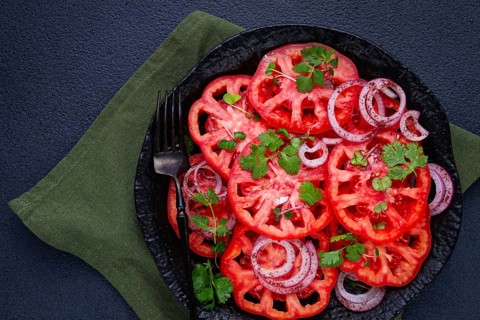 Freshly sliced tomatoes and red onions, garnished with herbs, on a black plate, summer salad, no