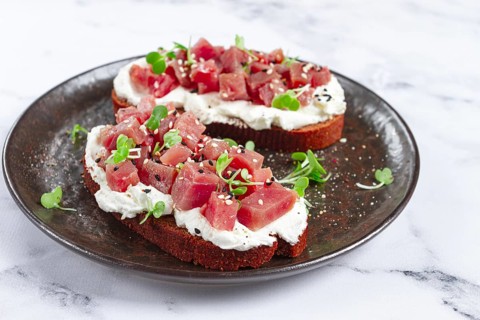 Sandwiches, rye bread with cream cheese, sliced tuna fillet with herbs, breakfast on a black plate,