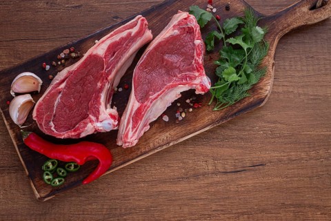 Freshly sliced lamb chops, with herbs and vegetables, on a wooden board, ready to cook, on a wooden