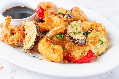 Shrimp and assorted vegetables are deep fried in a light batter and served on a white plate. A