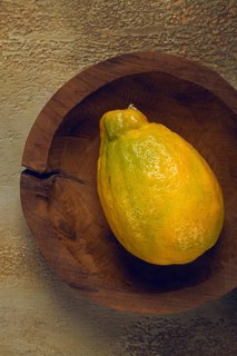 A vibrant yellow fruit, possibly a lemon or a ripe papaya, sits in a handcrafted wooden bowl