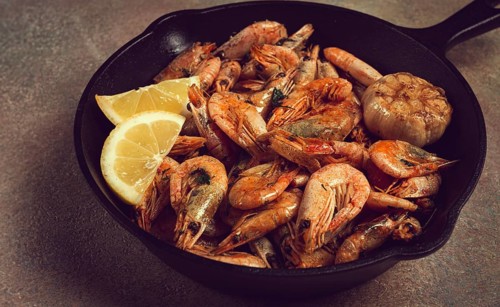 Fried shrimps, in a cast-iron pan, shrimps for beer, in a newspaper, on a gray table, there are no