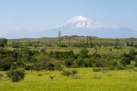 Green pasture with snow-covered mountain in the background and scattered huts, view of large and