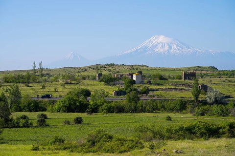 Wide green landscape with views of snow-capped mountains and scattered huts, view of large and
