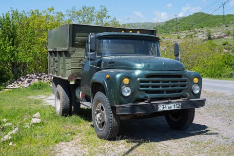 A green truck parked on a rural road surrounded by green trees, ZIL 130 truck powered by gas,