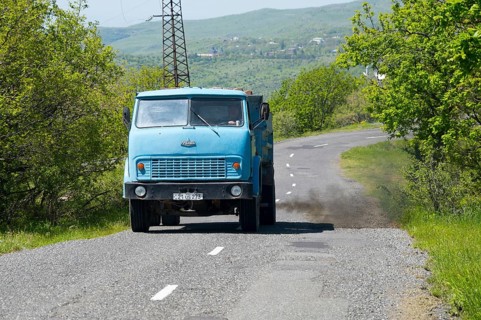 A blue truck drives on a winding country road through green hills, MAZ trucks, exhaust gases,