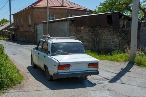 A rear view of an old car on a rural road surrounded by old buildings, Lada 2107, also WAS-2107,