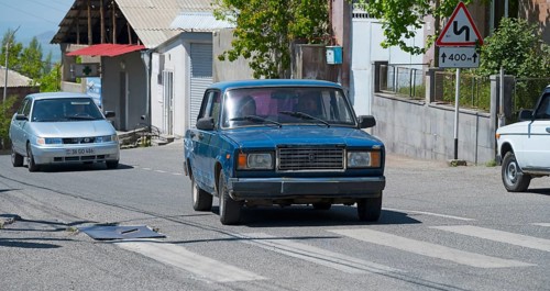 A blue car on a city street surrounded by road signs on a sunny day, Lada 2107, also WAS-2107,