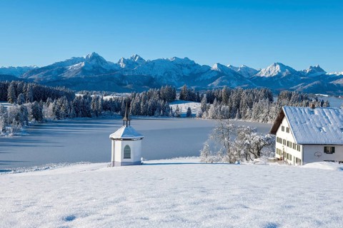 Snowy landscape with chapel, farm and mountains in the background under clear sky, Hegratsrieder