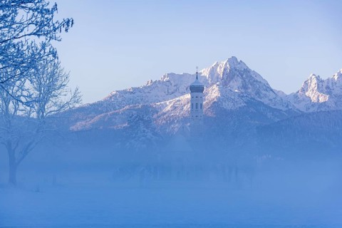Snowy mountain landscape with St. Coloman pilgrimage church in the foreground and foggy background,