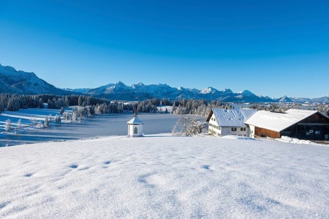 A winter landscape with farm and chapel in front of snowy mountains under a blue sky, Hegratsrieder