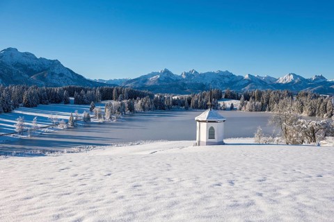 Snow-covered plain with a chapel and mountains under bright blue sky, Hegratsrieder See, near