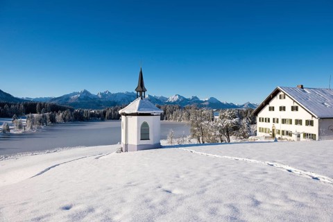 Winter scenery with chapel and house in snow-covered surroundings with mountain panorama,