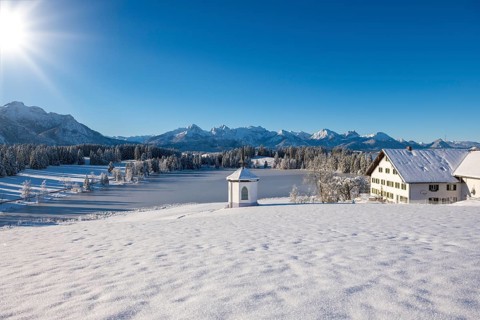 Snowy landscape with chapel, farmhouse and mountains under brilliant sunshine, Hegratsrieder See,