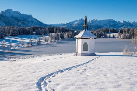 Small chapel in winter with footprints in the snow and mountains in the background, Hegratsrieder