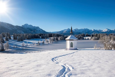 Chapel in snow with footprints and sunny mountain landscape, Hegratsrieder See, near Füssen,
