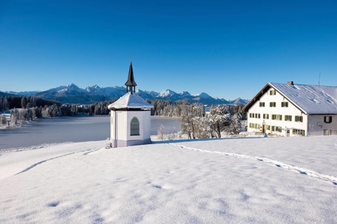 Chapel and farmhouse in snowy landscape with mountains in the background, clear atmosphere,