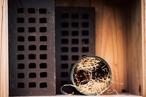 Insect hotel, nesting aid for wild bees made of perforated bricks and can with straw and pine cones