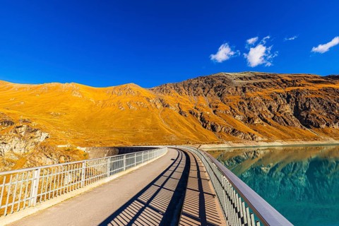 The dam of the Lac de Moiry reservoir, behind alpine meadows in autumn colors, Val d'Anniviers,