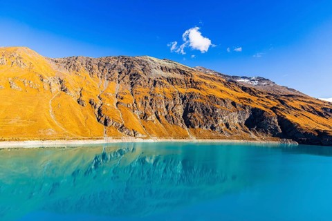 Steep and rocky mountain slopes are reflected in the La de Moiry Reservoir, Val d'Anniviers, Valais