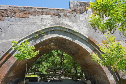 View of an old stone bridge structure against a wooded background on a sunny day, part of a