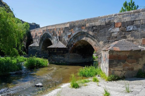 Old stone bridge with several arches across a small river surrounded by lush nature and green