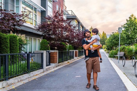 Father carrying his son while walking on a sidewalk in a residential area of vancouver, british