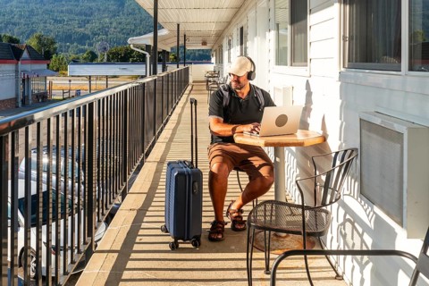 Male digital nomad wearing headphones and working on laptop while sitting at table on motel balcony