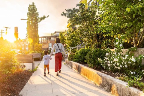 Mother and son are walking hand in hand down a sidewalk in a residential neighborhood of vancouver,