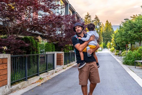 Father carrying his son is walking down a residential street in vancouver, british columbia,