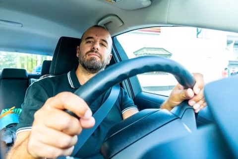 Caucasian man driving a modern car, wearing a seatbelt and holding the steering wheel, driving in