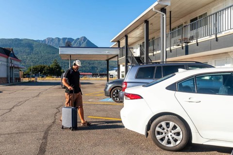 Male tourist wearing headphones and carrying a backpack strolls through a parking lot, pulling a