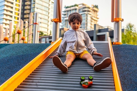 Young boy sitting on a playground slide in vancouver, british columbia, playing with a toy car
