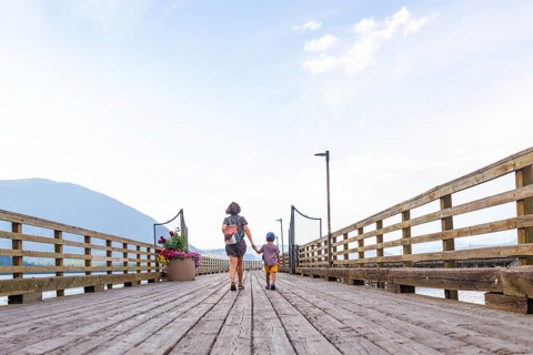 Mother and son holding hands are enjoying a leisurely stroll along a picturesque wooden pier in