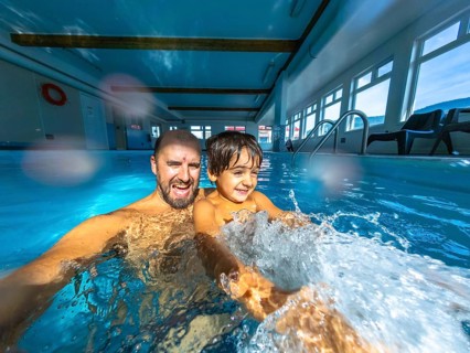 Father and son enjoying playful moments while splashing in an indoor swimming pool, creating a