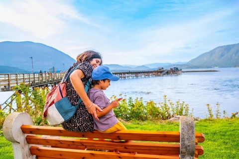 Mother and her son are sitting on a bench, enjoying the scenic view of shuswap lake and the public