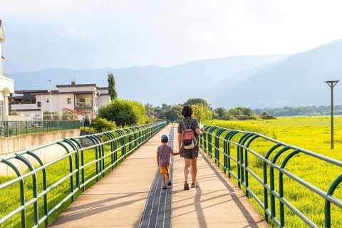 Mother and son enjoying a leisurely stroll on a pedestrian bridge, surrounded by lush greenery and