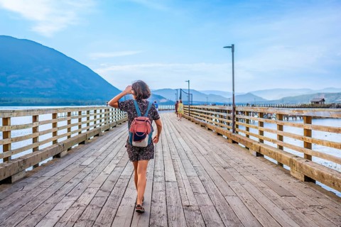 Young woman with backpack walking down a long wooden pier, enjoying the scenic view of the shuswap