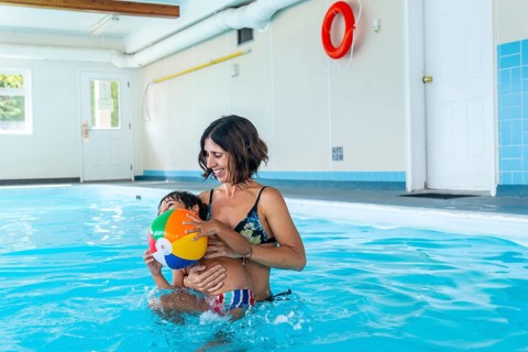 Mother holding her son while playing with a vibrant inflatable beach ball in an indoor swimming