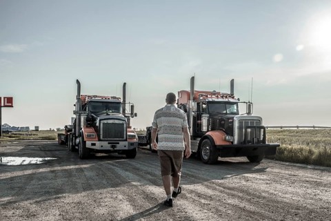 Trucker walking towards two semi trucks parked on a gravel road near hemlock grove boardwalk in the