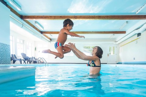 Smiling young mother catching her cheerful son as he leaps joyfully into the indoor swimming pool,