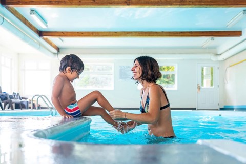 Happy mother and son enjoying playful moments at the edge of an indoor swimming pool, splashing