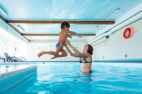 Smiling mother catching her joyful son mid air as he jumps into the pool, enjoying a playful moment