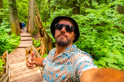 Happy tourist wearing sunglasses and bucket hat taking a selfie while hiking the beautiful giant