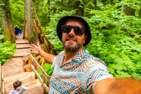 Happy tourist wearing sunglasses and a bucket hat taking a selfie while walking the giant cedars
