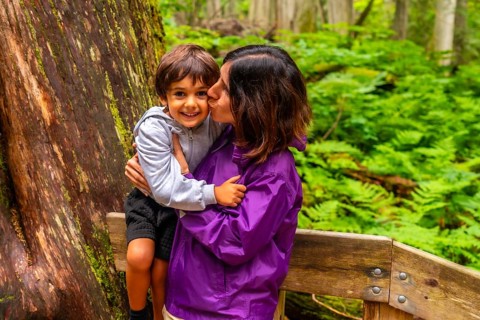 Mother kissing her smiling son while hiking the giant cedars boardwalk trail in mount revelstoke