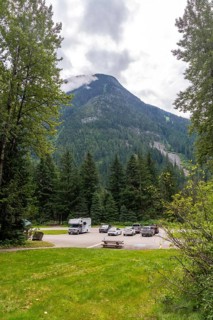 Clouds partially covering mountain peak near parking lot with parked recreational vehicles and cars