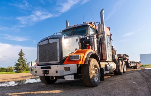 Gleaming orange and silver semi truck parked on a gravel road, bathed in the warm glow of late